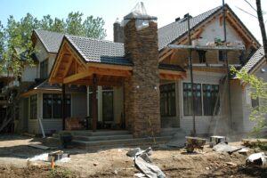 Custom home under construction showing timber framing and stacked-stone chimney detail